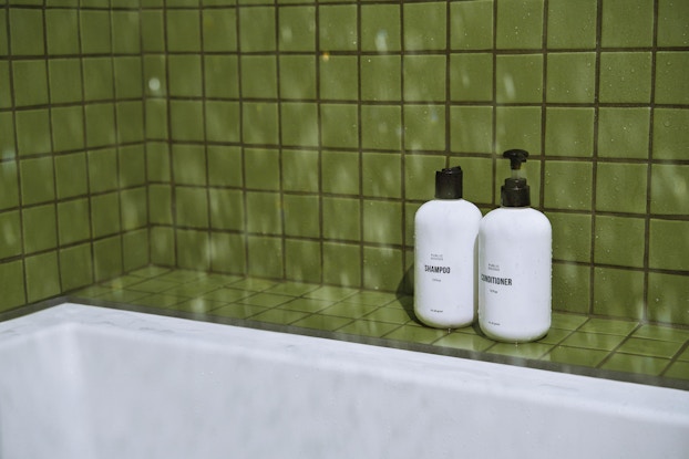  Bottles of shampoo and conditioner by Public Goods in a bathroom shower lined with green tiles.