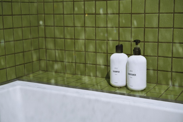 Bottles of shampoo and conditioner by Public Goods in a bathroom shower lined with green tiles.