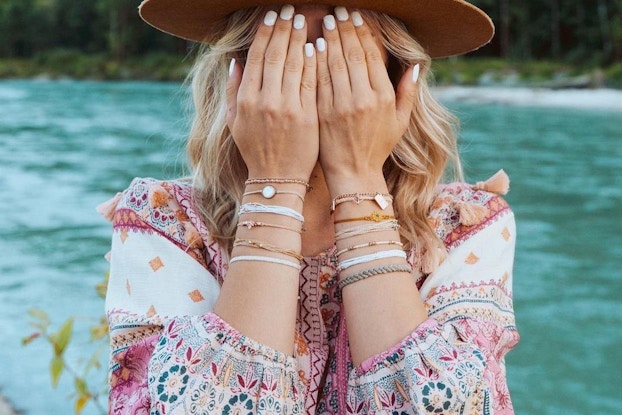  Influencer wearing Pura Vida bracelets and covering her eyes while outside in nature.