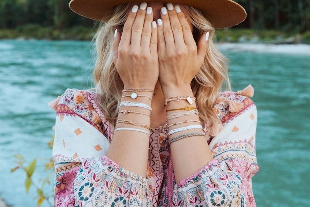 Influencer wearing Pura Vida bracelets and covering her eyes while outside in nature.