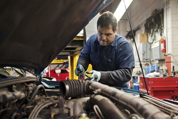  Car repair mechanic working under the hood of a car.