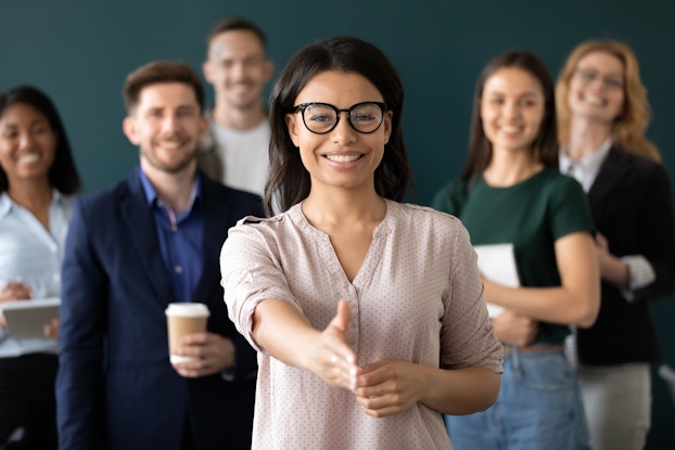  woman at the forefront of a group of people with a hand out to shake hands for a job interview