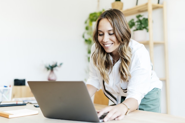  Woman smiling at her laptop while working remotely.