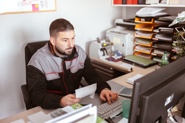 A car service technician enters an invoice into his shop's computer system.