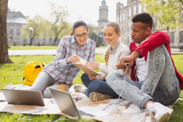 group of college students sitting on lawn with laptops