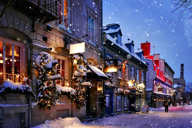 Snowy sidewalk displaying a row of storefronts decorated for the holidays.