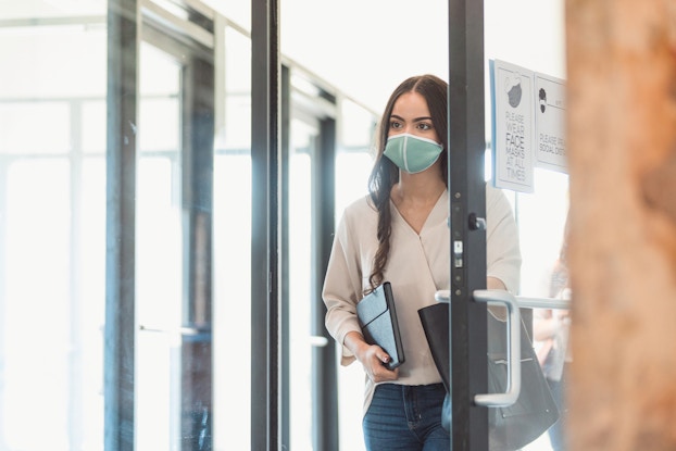  During the COVID-19 pandemic, female wears masks to attend work. On the door of the are signs encouraging mask wearing a social distancing.