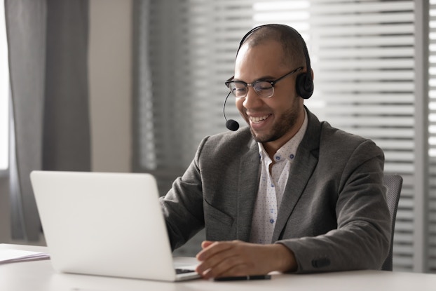 A man wearing a headset sits in front of a laptop.