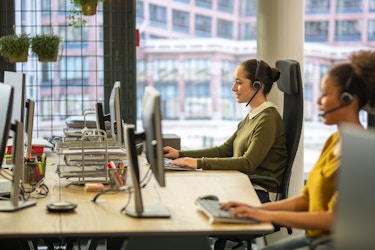 two coworkers working on laptops on headset