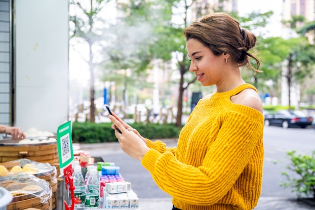 Woman in bright yellow sweater scanning a QR code with her phone.