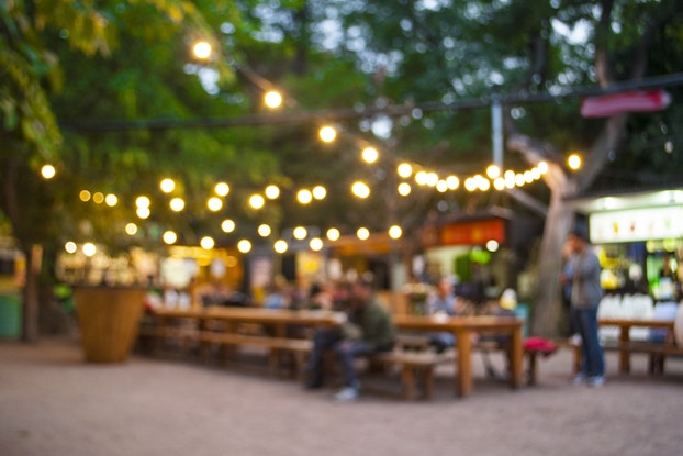 Blurred outdoor social area with picnic tables and bistro lights.