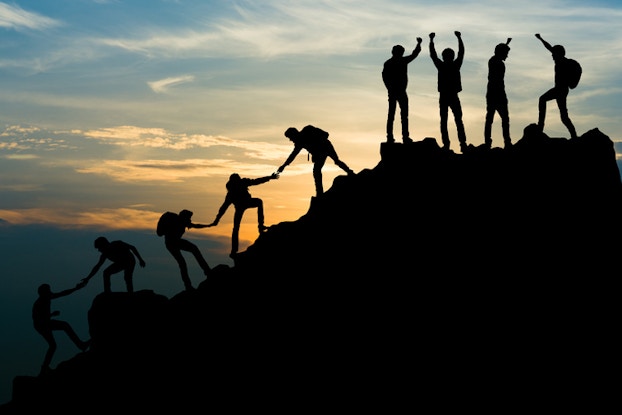  people helping each other climb a mountain