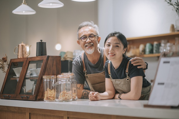  Father and daughter business team standing behind a cafe counter.