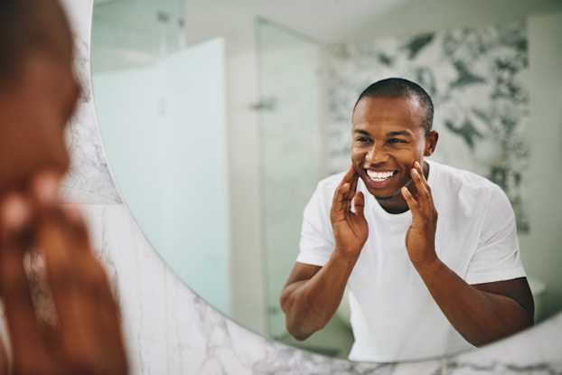 man looking in mirror touching his face