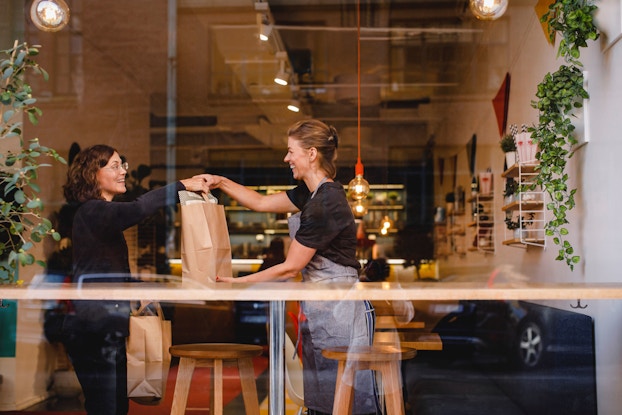  An outside view of a smiling saleswoman handing a shopping bag to a female customer at checkout.