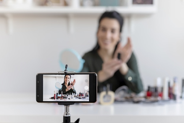  A smartphone on a tripod takes a video of a woman showing off various beauty products.