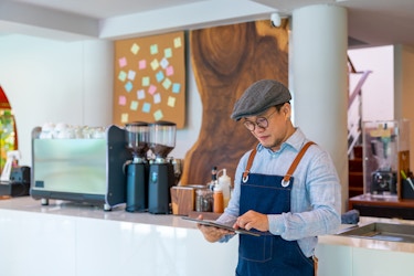 Coffee shop owner inside shop on tablet.