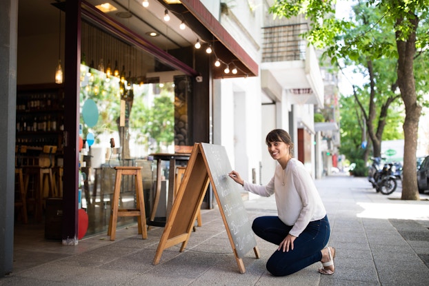 woman outside shop writing on chalkboard
