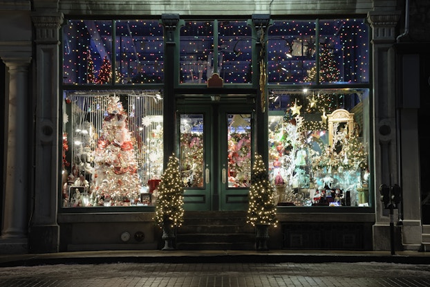  Exterior of a shop where you can see holiday lights and decor set up inside.