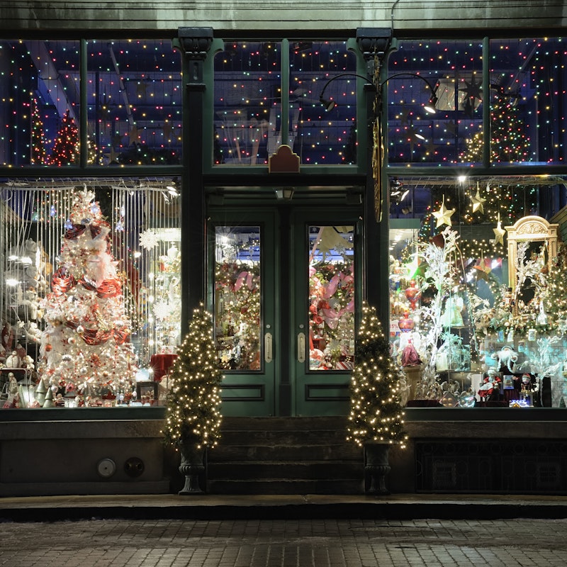Exterior of a shop where you can see holiday lights and decor set up inside.
