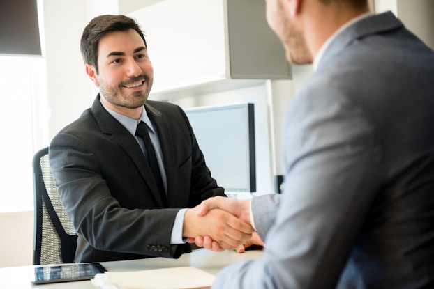 A businessman who is interviewing for a sales role shakes hands with the interviewer.