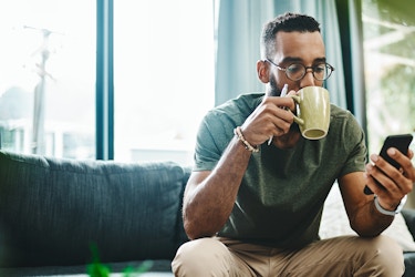  man drinking coffee looking at cellphone 