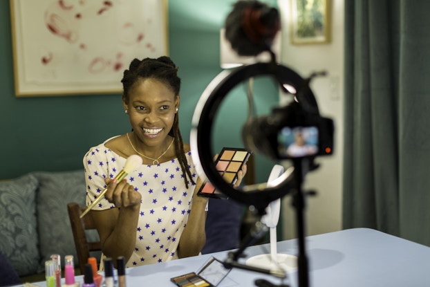 Smiling woman recording herself putting on makeup for a video.