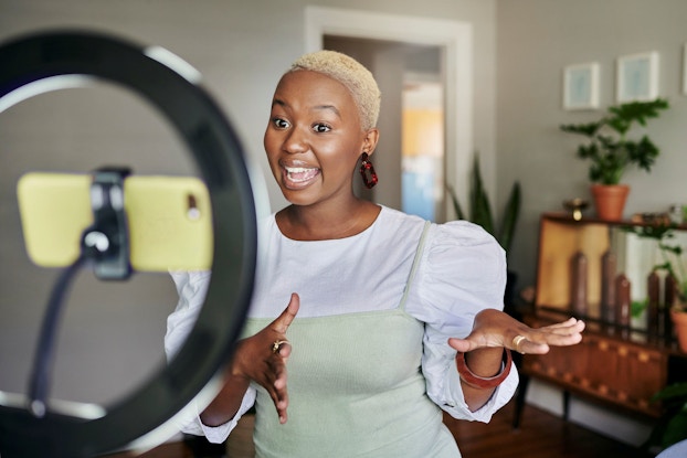  A young, smiling small business owner uses her smart phone to conduct a Facebook live video.