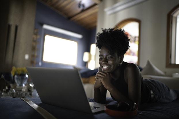  woman smiling while laying down looking at her laptop screen