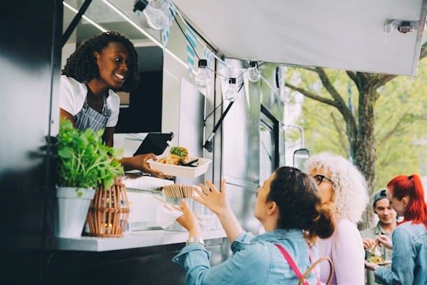  A woman business owner of a popular food truck hands a customer her order.