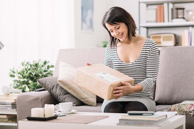 Happy woman holding a package while sitting on the couch.