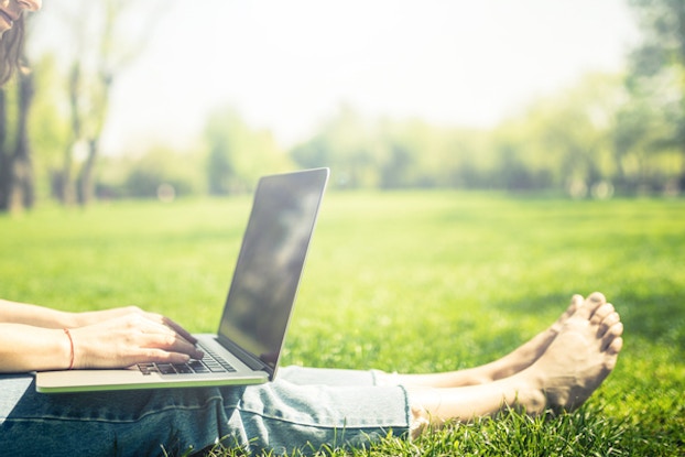  woman sitting in grass on laptop