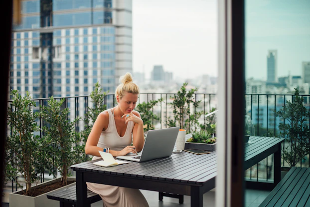 Woman working on her laptop outside on her balcony.