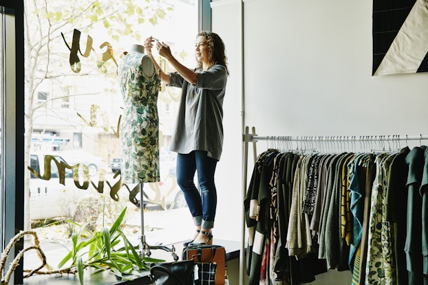 Business owner dressing a mannequin in her shop window.