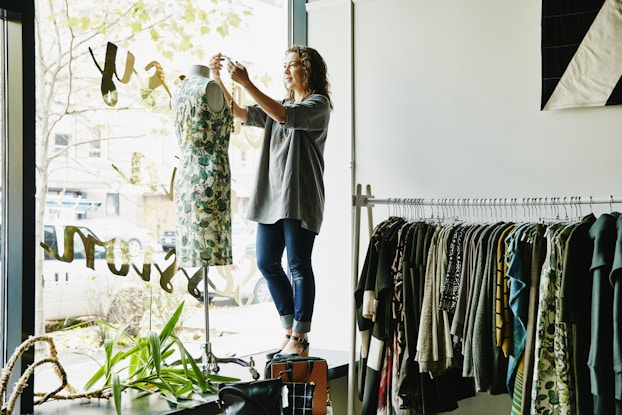  Business owner dressing a mannequin in her shop window.