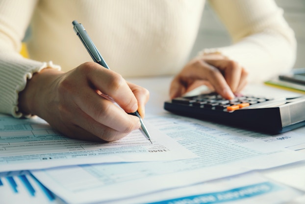  Close-up on a pair of hands. One hand uses a mechanical pencil to fill out a form while the other presses buttons on a calculator.