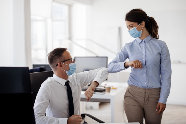 coworkers wearing masks bump elbows in office