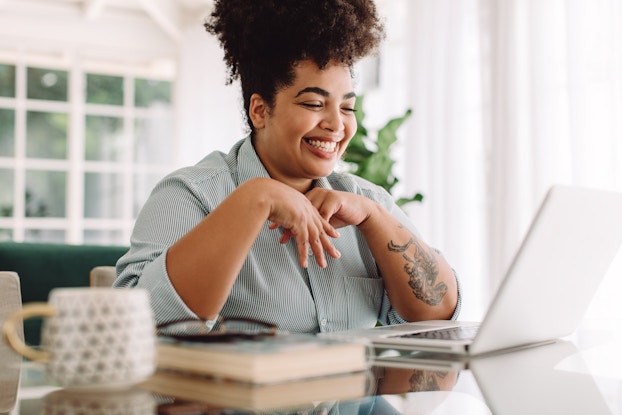  Person smiling at laptop while sitting at a desk working from home.