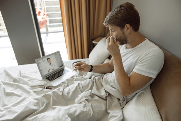  man sick in bed on laptop with telehealth doctor