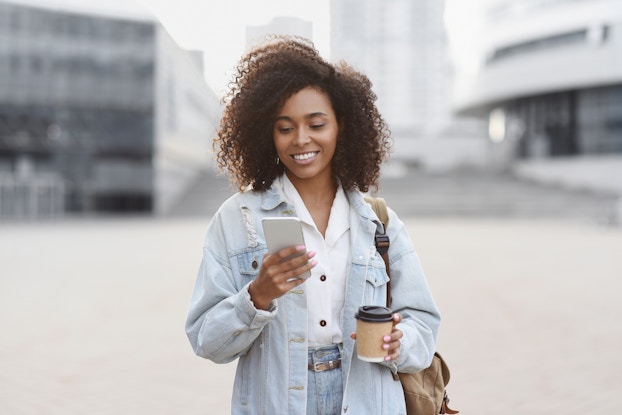 Woman outside holding a coffee and looking at her phone.