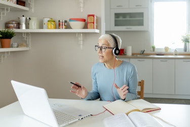  woman working from home talking on headset at dining room table 