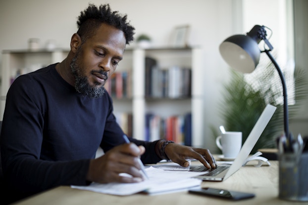  Person sitting in a home office writing with a pen and paper.