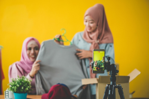  Two women modeling clothing for a video being recorded on a smartphone.