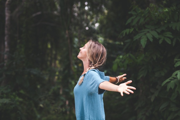 woman standing in nature with her head up and arms out