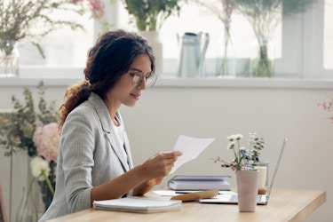  Woman sitting at a desk wearing eyeglasses and going over paperwork. 