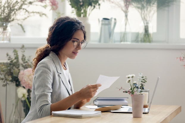  Woman sitting at a desk wearing eyeglasses and going over paperwork.
