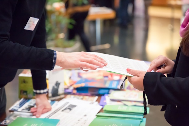 A close-up photo features the hands of a man and a woman that are reviewing a document and exchanging information at an exhibition.