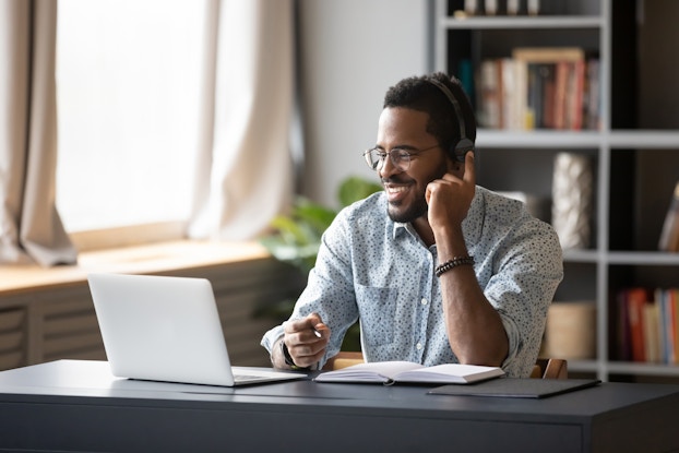 Person working on laptop at home wearing a headset and smiling.