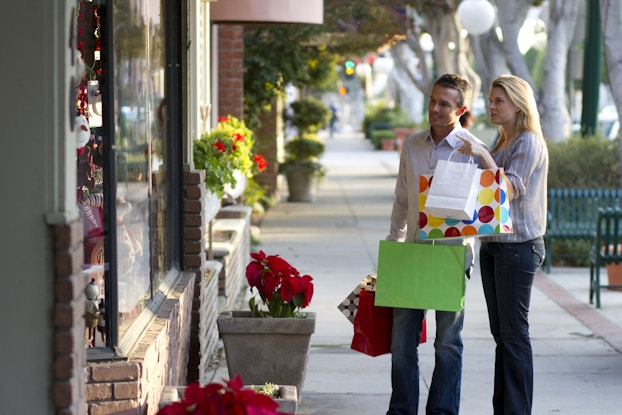 Two people walking through a small town holding shopping bags and looking in store windows.
