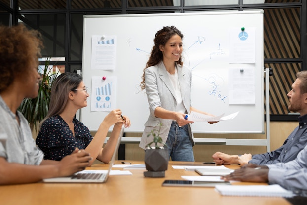 woman presenting to coworkers in a meeting in front of a whiteboard